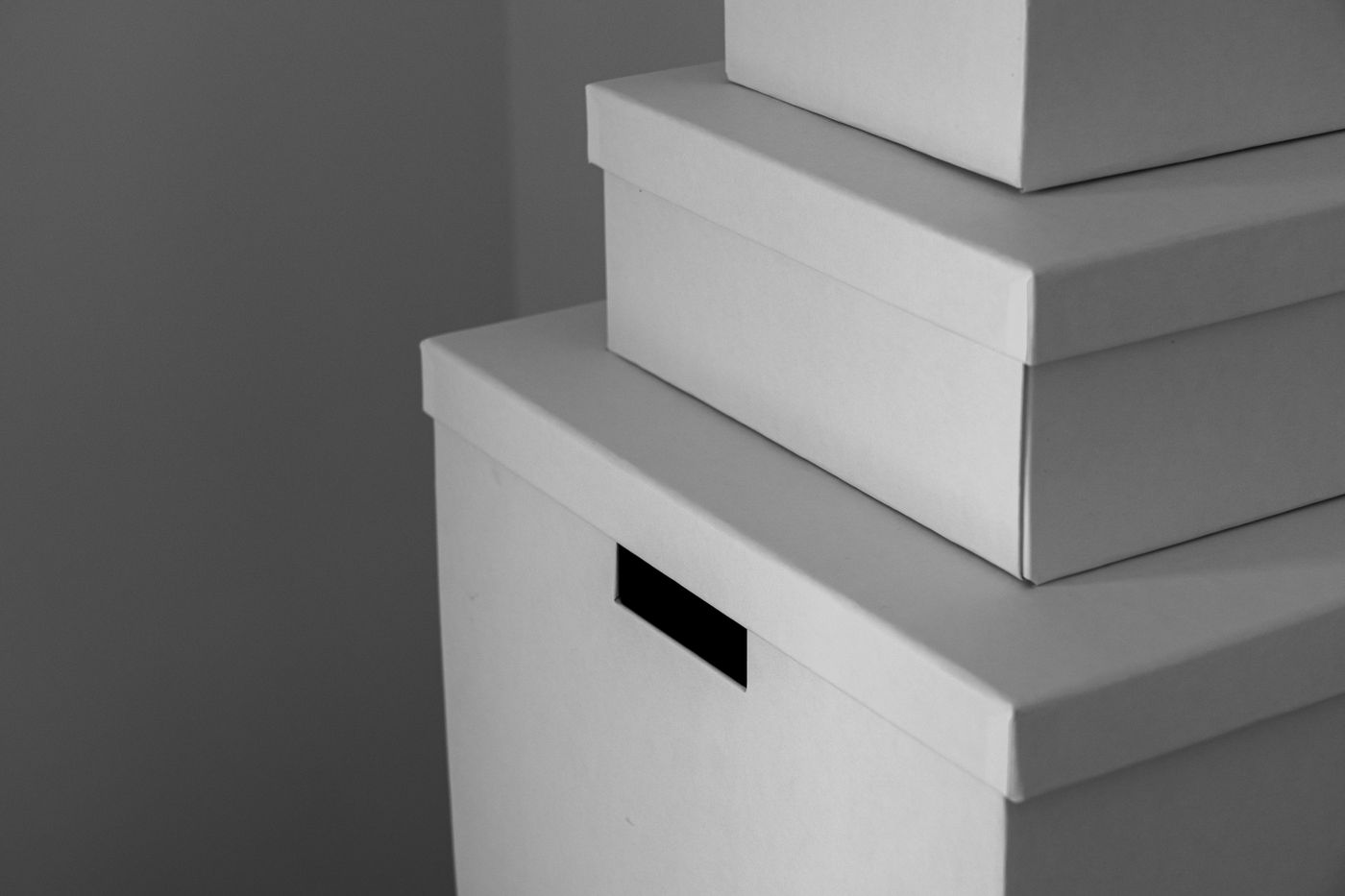 Nahaufnahme von drei schlichten weißen Aufbewahrungsboxen mit Deckel, gestapelt vor einer mittelgrauen Wand; Seitenlicht trennt jeden Deckel von der Box darunter.