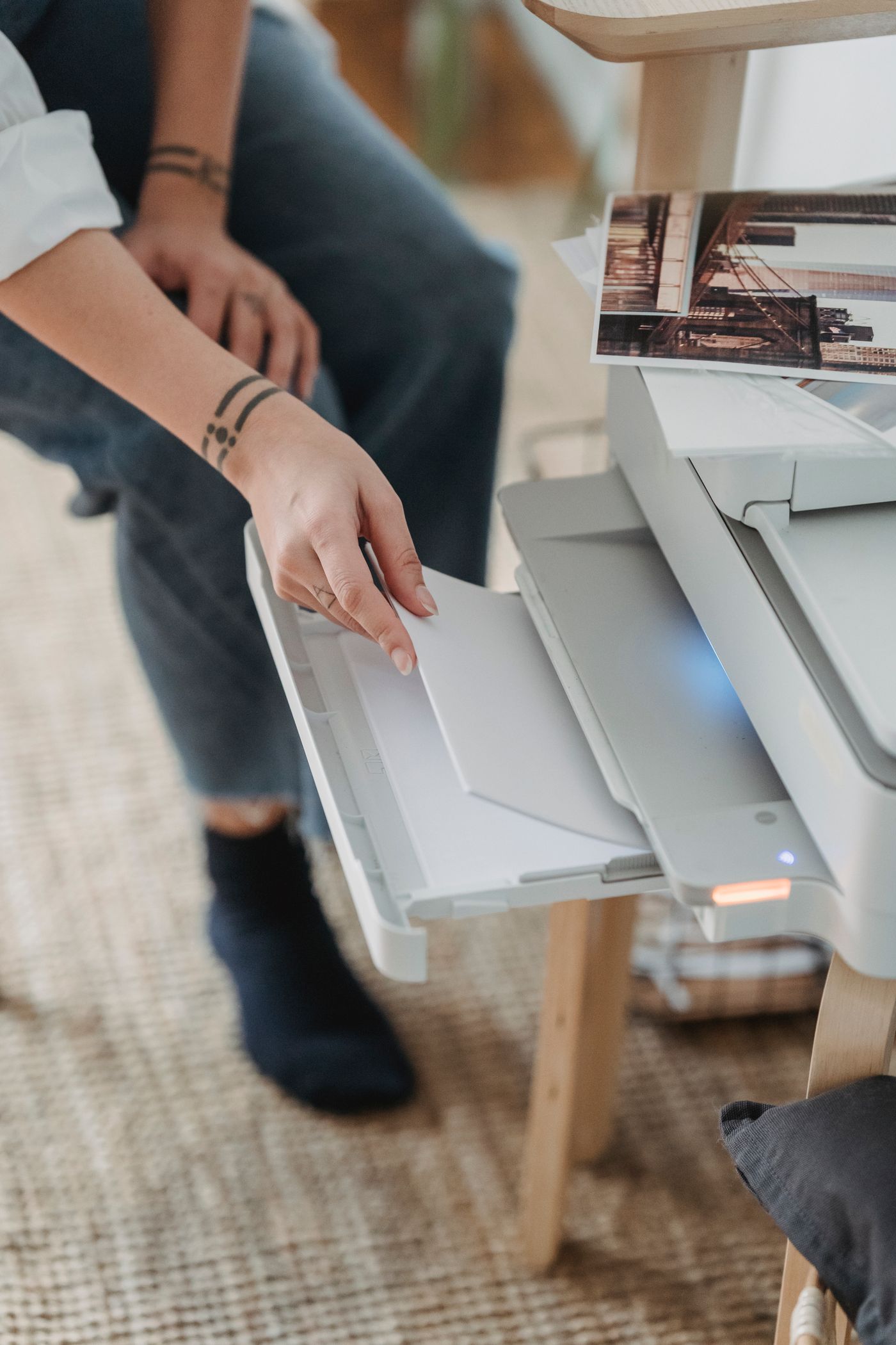 Overhead view of a person's hands sliding a stack of blank sheets into the paper tray of a desktop home printer.