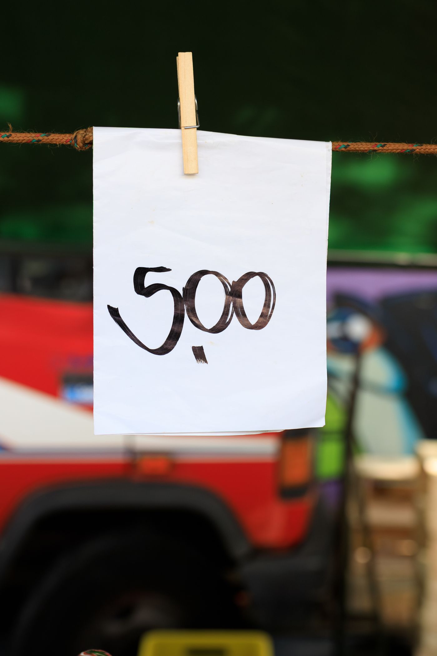 A sheet of white paper printed with a single large number 500 pegged to a line at an outdoor market, with a red vehicle blurred behind it.