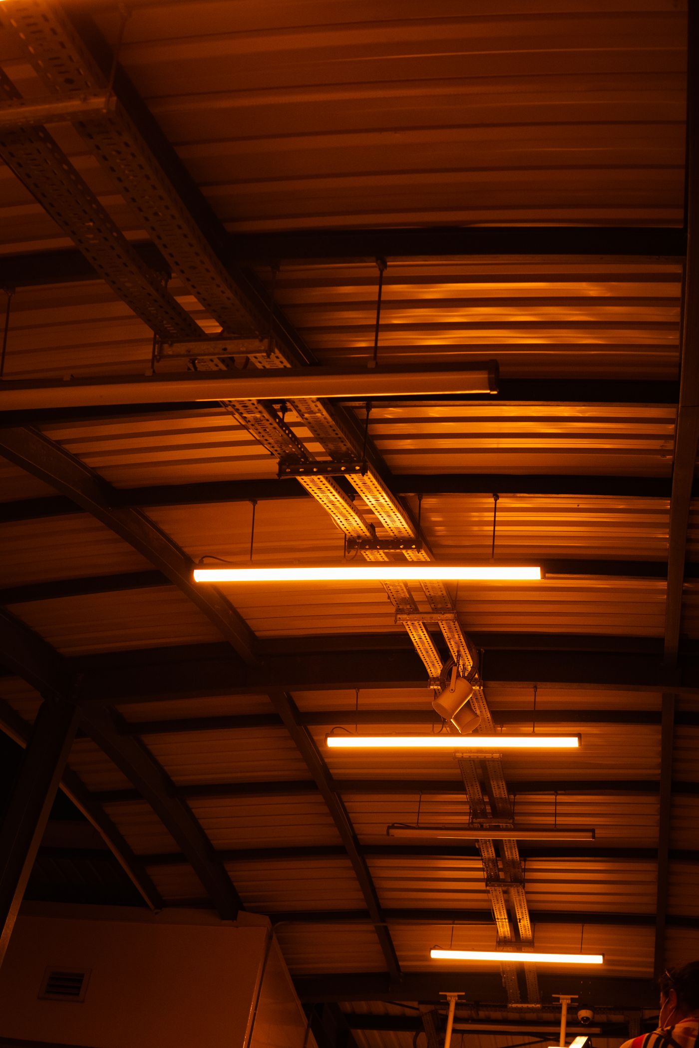 Low-angle view of glowing tube lights running in warm rows across a corrugated industrial ceiling.