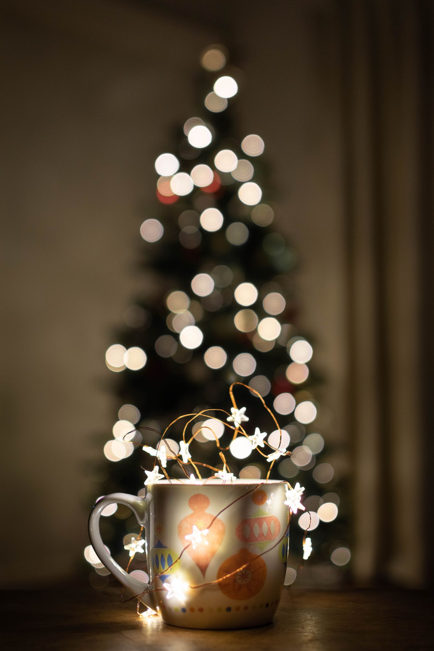 A ceramic mug cutout composited onto a cozy holiday backdrop with warm string lights and pine branches