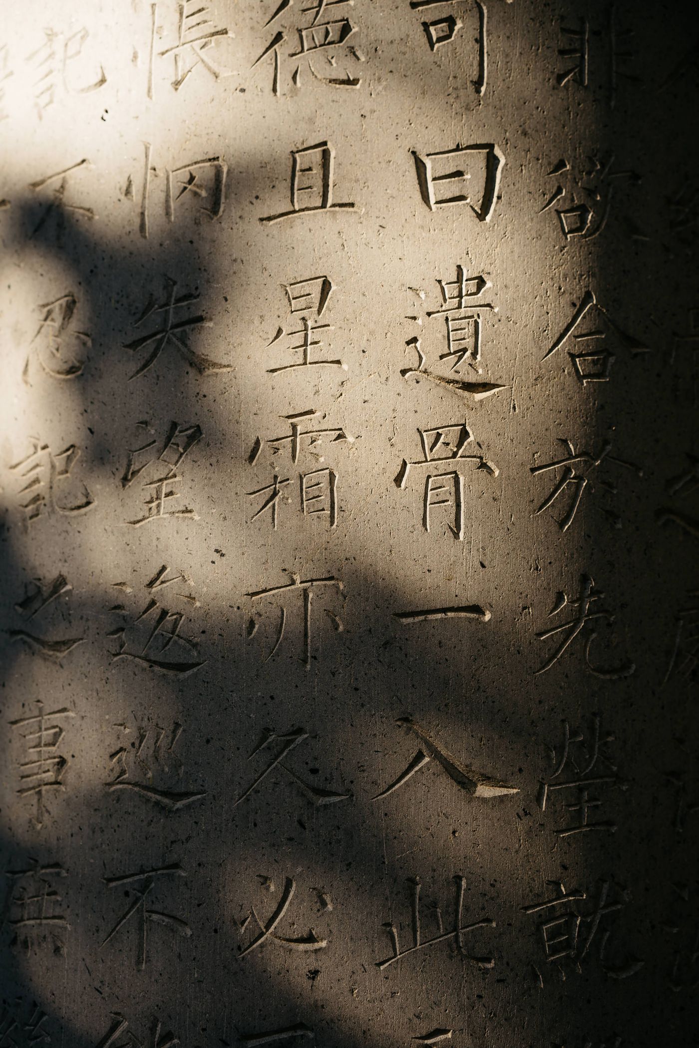 Close-up of characters carved into a pale stone tablet, lit from one side so each incised stroke casts a hard shadow