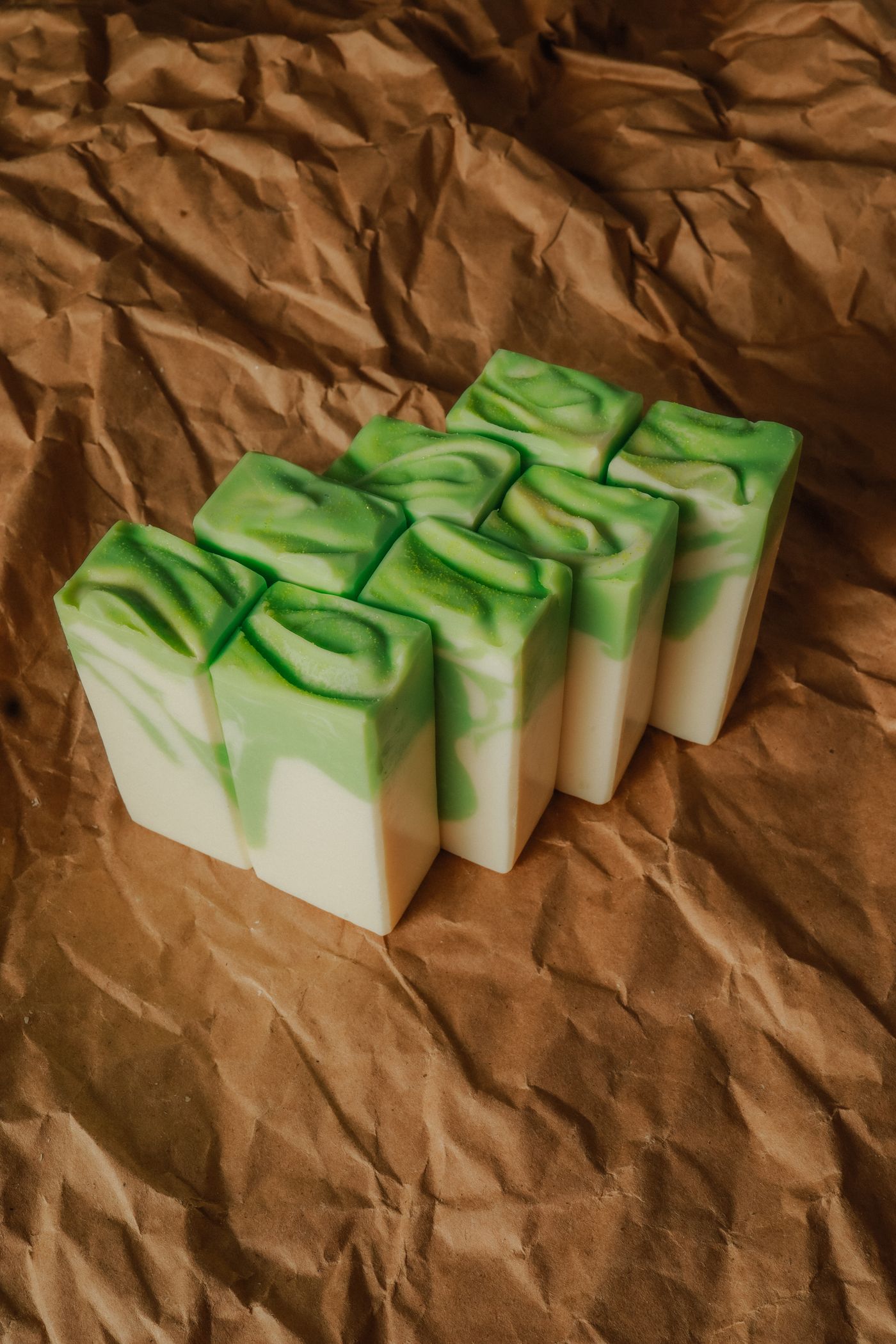 A tightly packed block of handmade soap bars standing upright in two rows on crumpled brown kraft paper, each one cream at the base with a green and white swirled top.