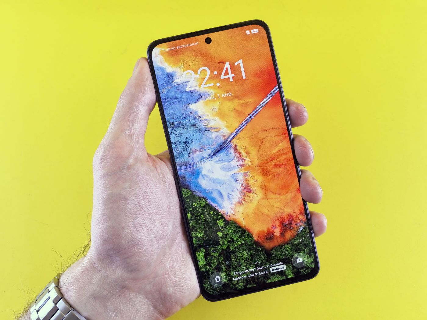 A hand holding a smartphone displaying a vibrant, colorful app interface against a bright solid-color background