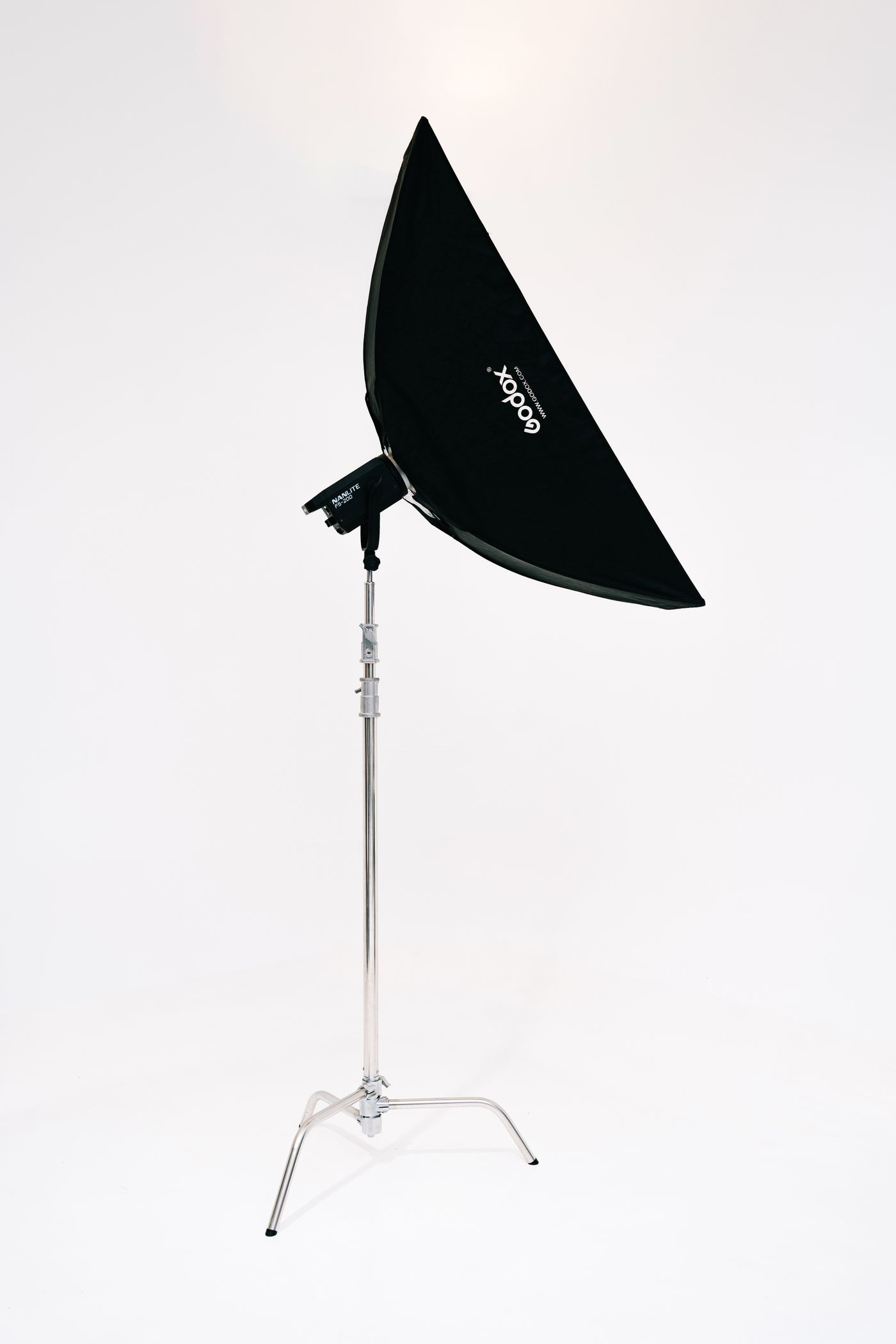 Um softbox retangular preto montado em um tripé de iluminação metálico, preparado para fotografia de estúdio diante de um fundo liso