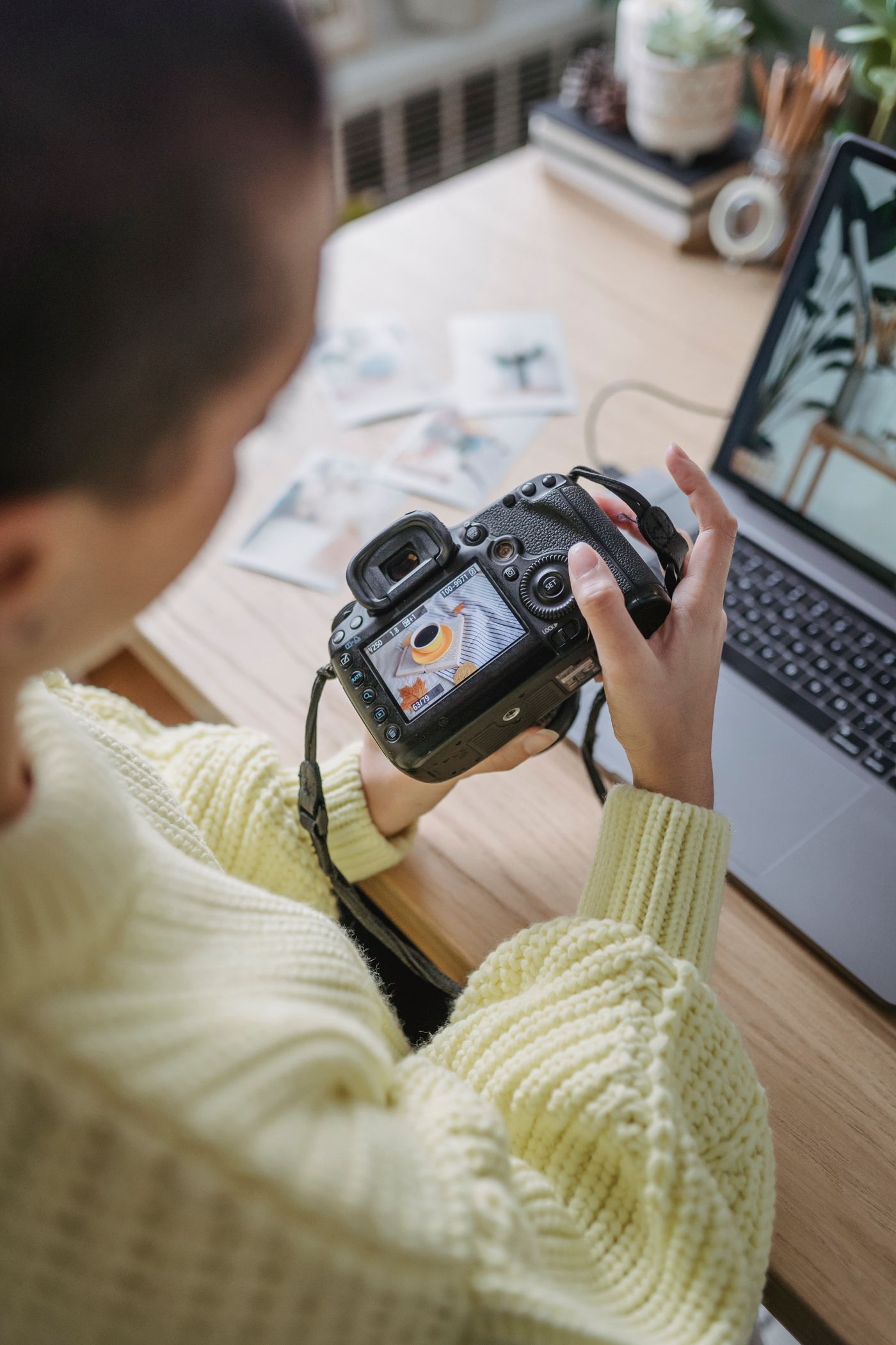 Widok z góry na fotografkę siedzącą przy stole, która sprawdza klatkę na tylnym ekranie aparatu, z otwartym laptopem obok