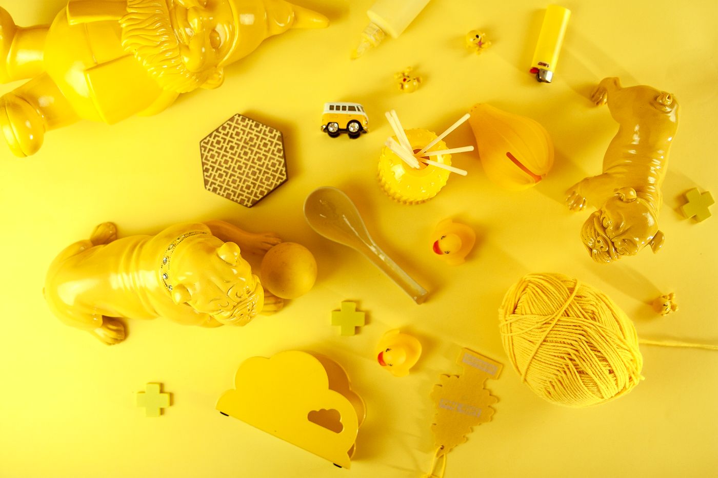 Flat lay of many unrelated yellow objects — rubber ducks, a garden gnome, bulldog figurines, a spoon and small souvenirs — arranged on a single bright yellow background