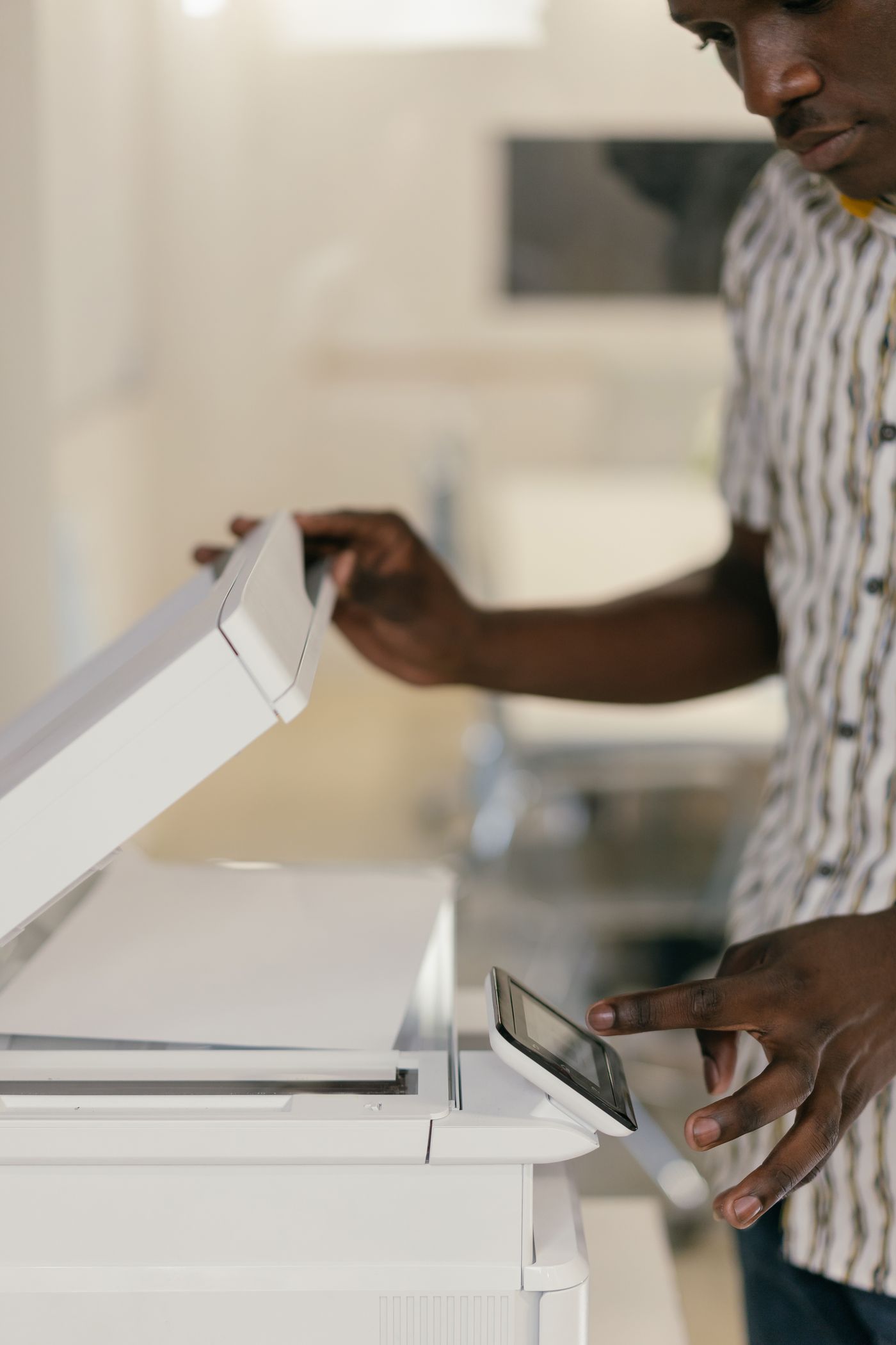 A man lifting the lid of an office photocopier with one hand while pressing the control panel with the other