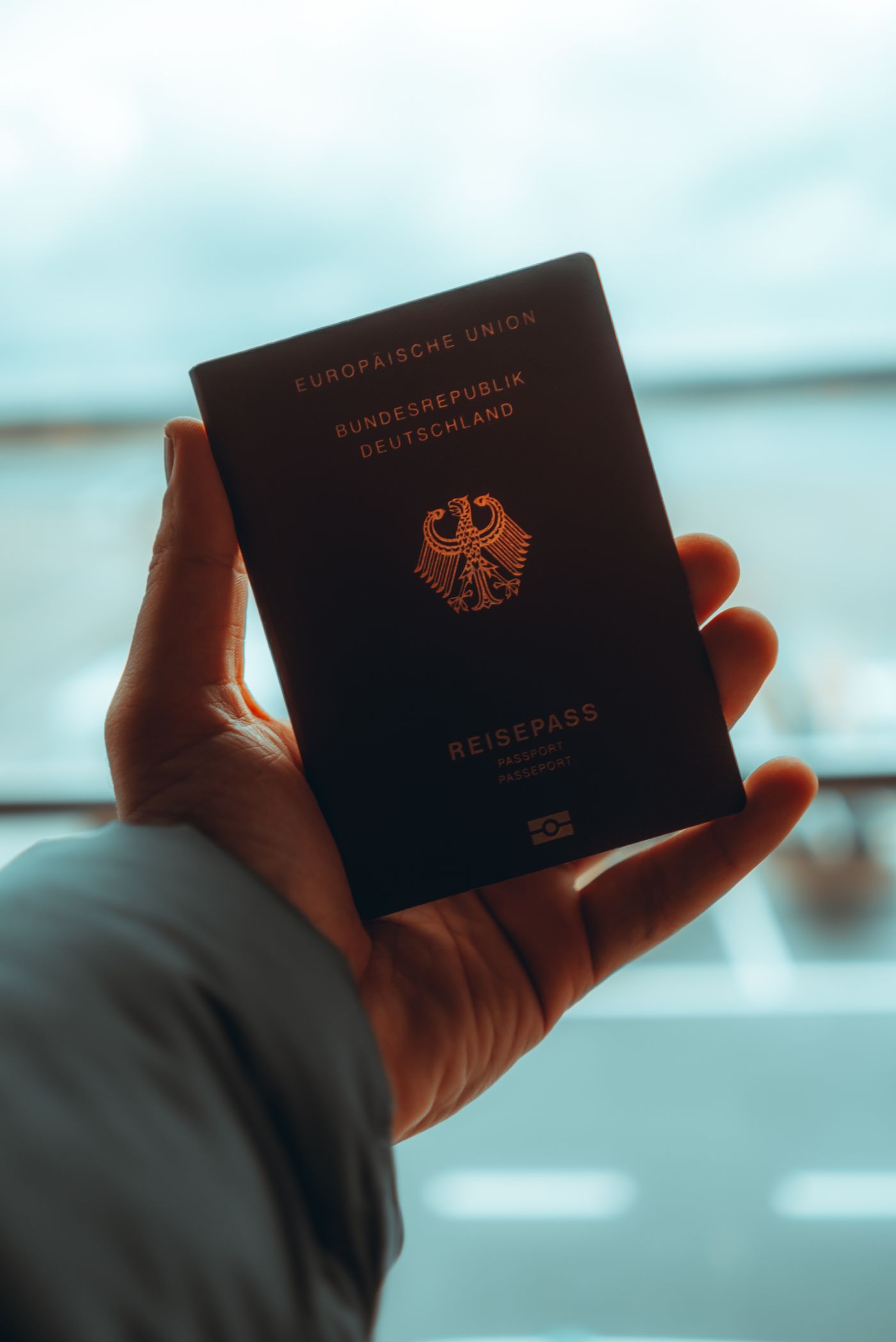 Zbliżenie dłoni trzymającej bordowy niemiecki paszport, na okładce widać federalnego orła i symbol chipa biometrycznego