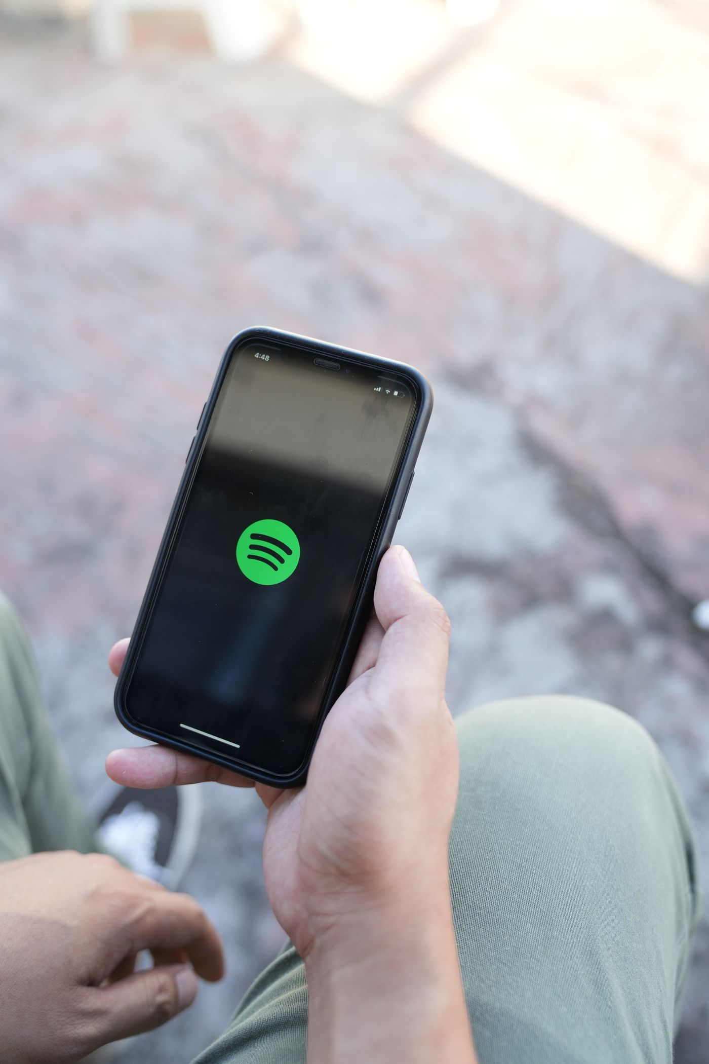 Dışarıda oturan bir kişi, siyah açılış ekranında yeşil Spotify logosunu gösteren bir akıllı telefon tutuyor