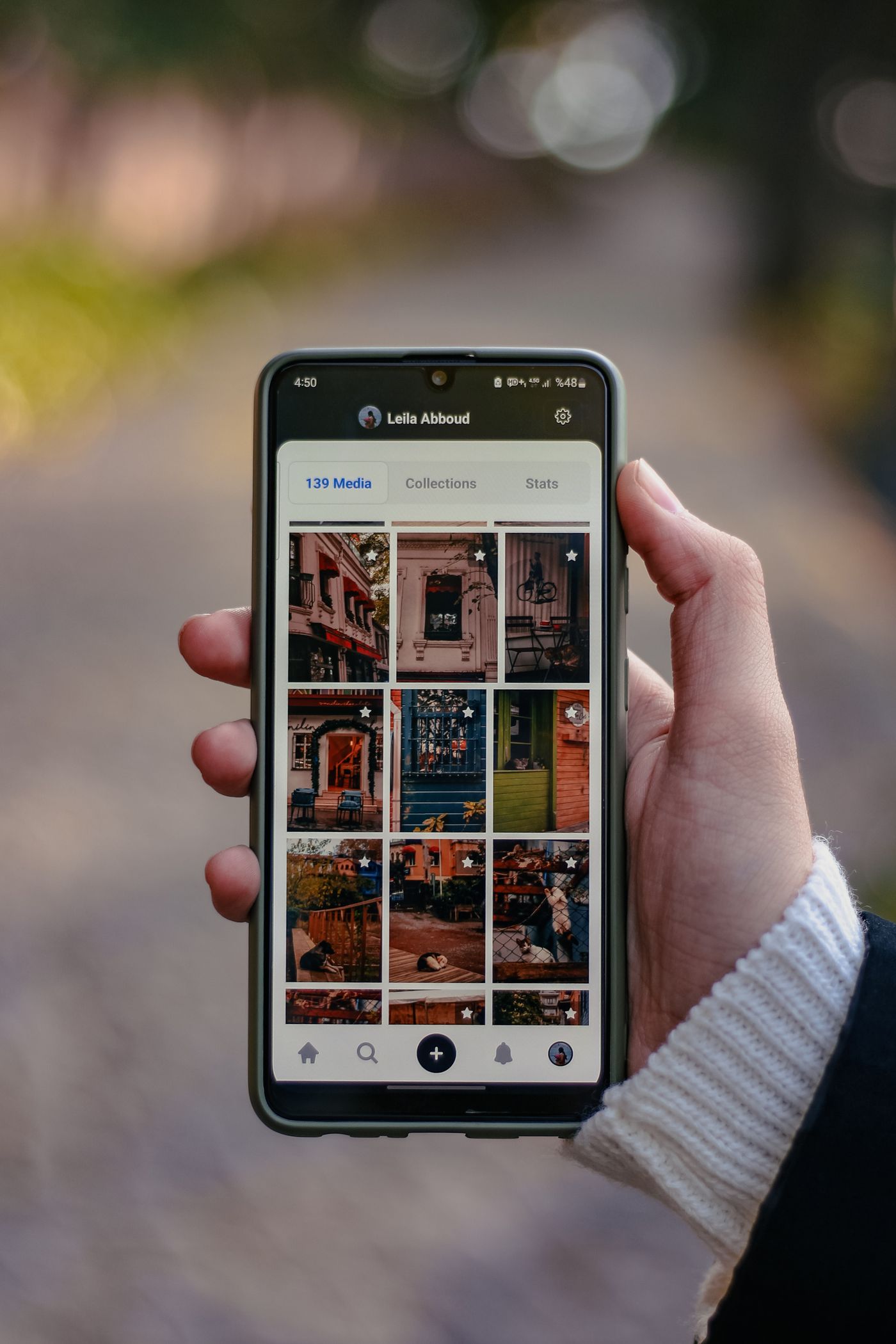 A hand holding a smartphone outdoors, its screen showing a photo gallery app full of pictures