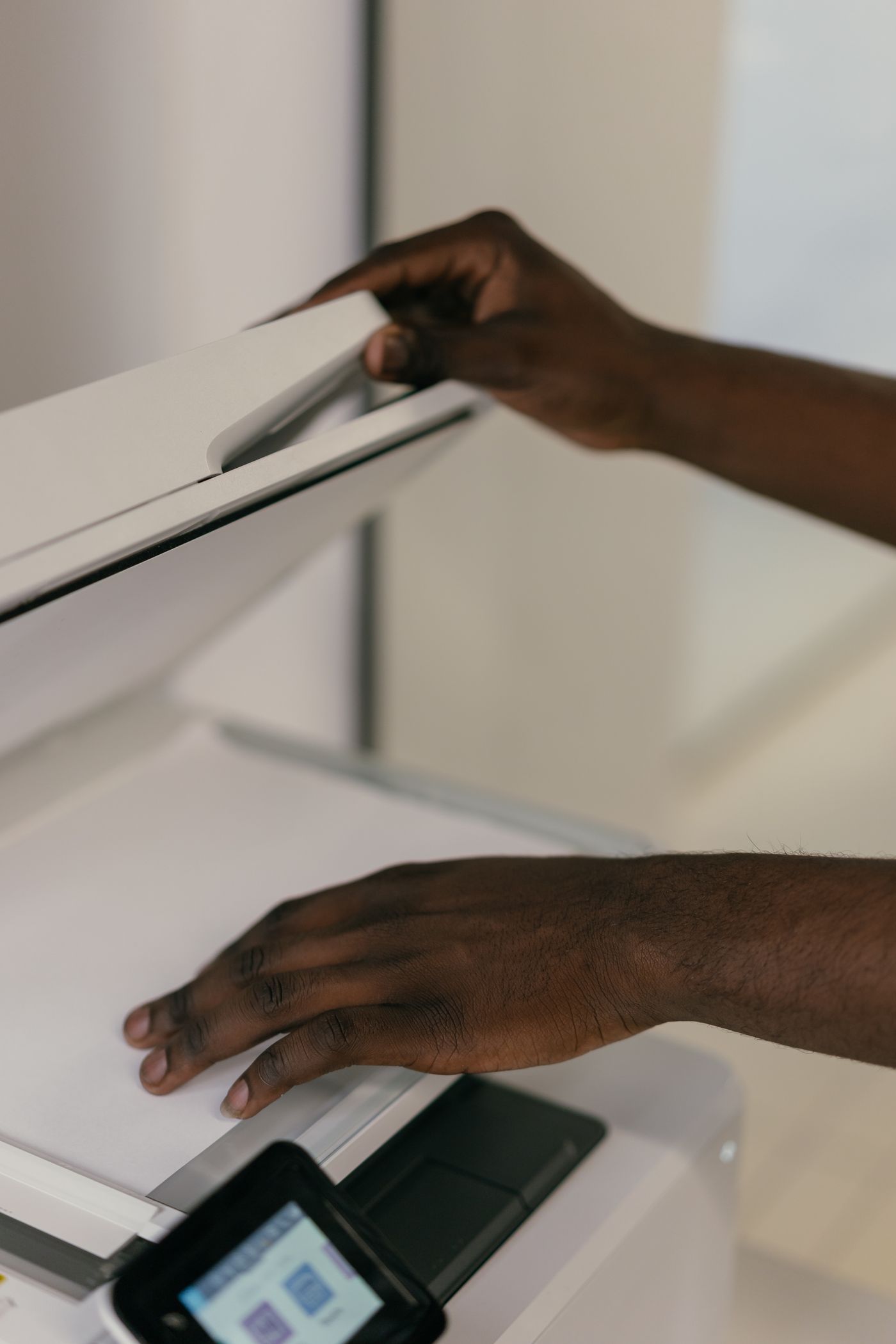 Hands lifting the lid of an office copier and laying a sheet of white paper face down on the glass