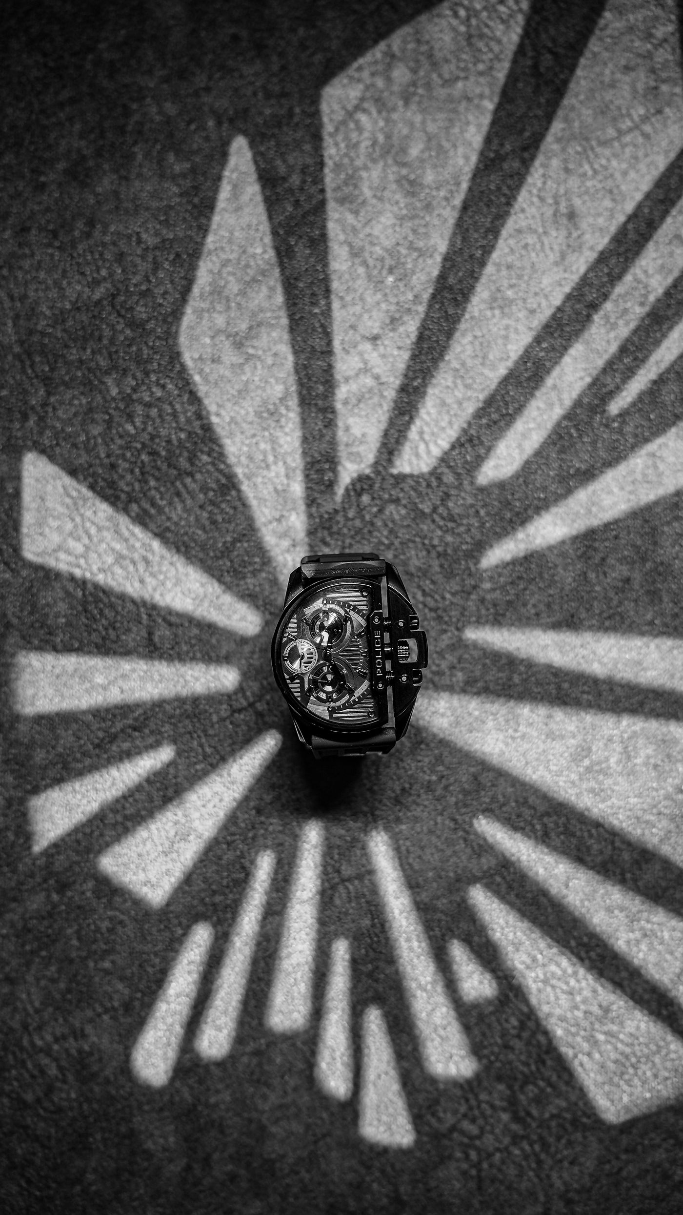 A wristwatch lit by a single hard light source casting a long crisp-edged shadow across a dark surface