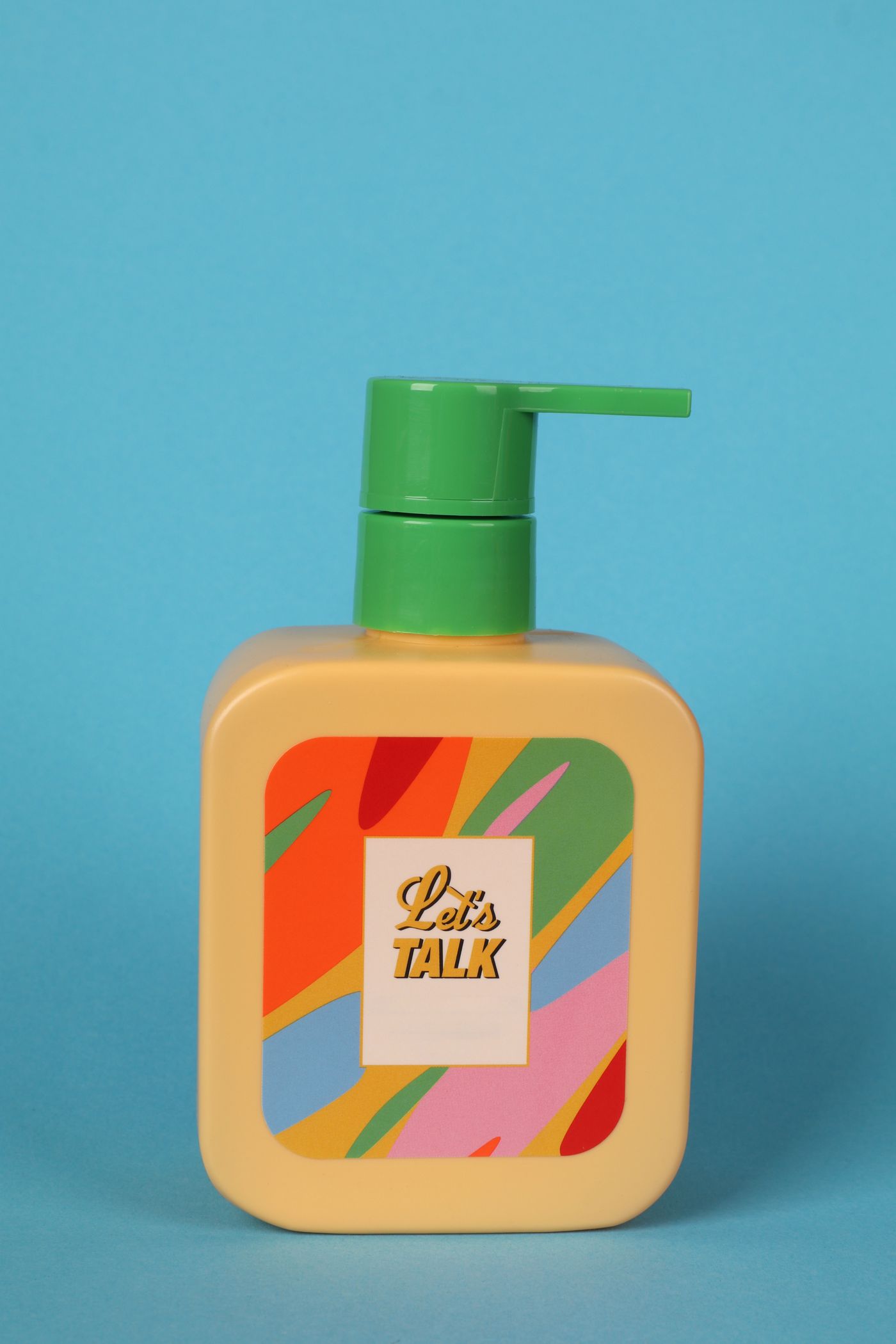 A colourful soap dispenser bottle photographed against a saturated blue backdrop in a styled studio setup.