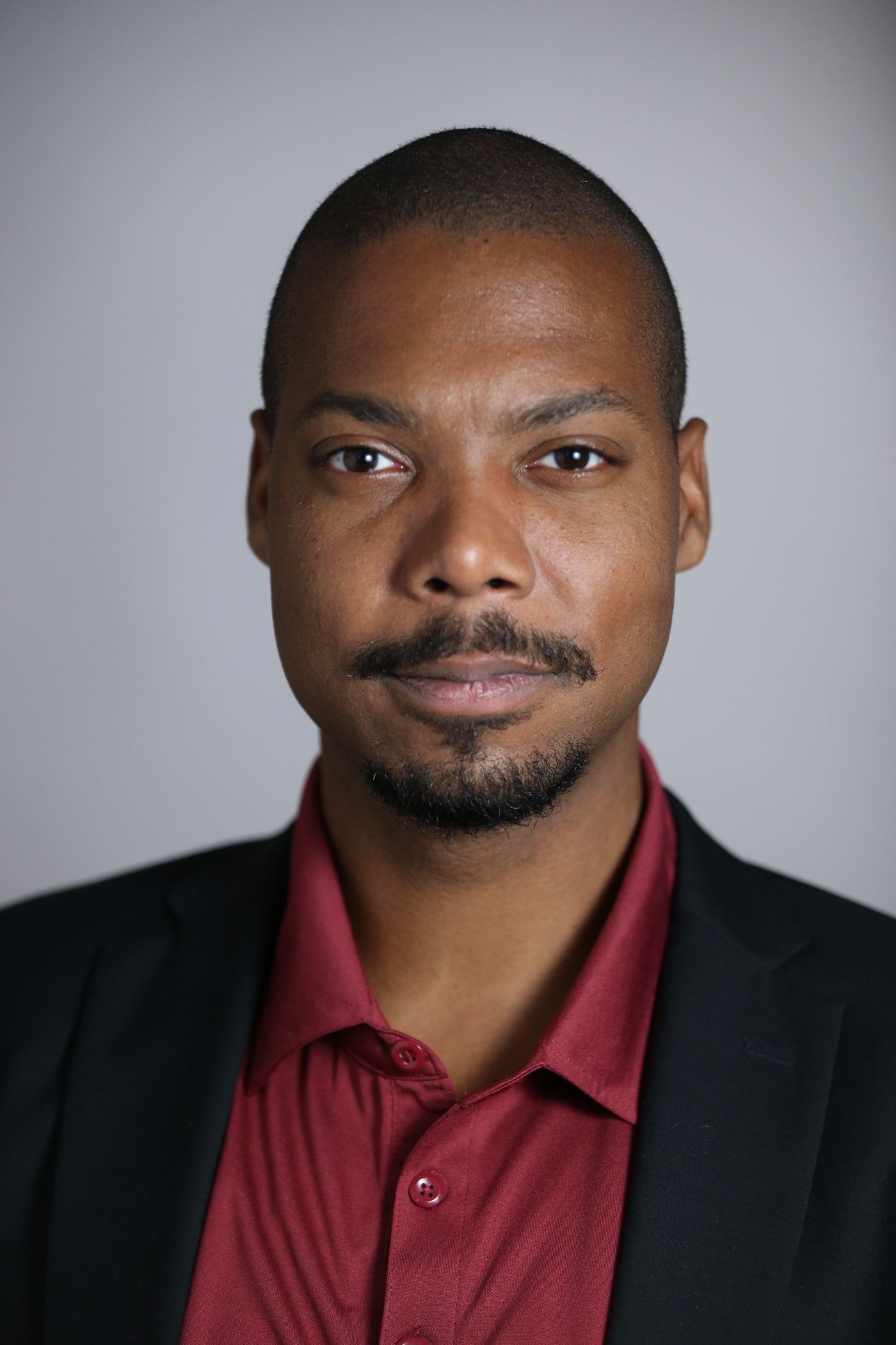 A professional resume headshot with head-and-shoulders framing, business attire, and a plain light gray background.