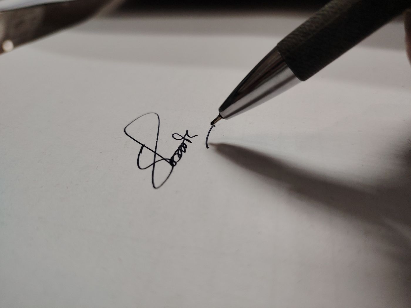Close-up of a black-ink pen finishing a looping handwritten signature on a plain, unlined sheet of white paper