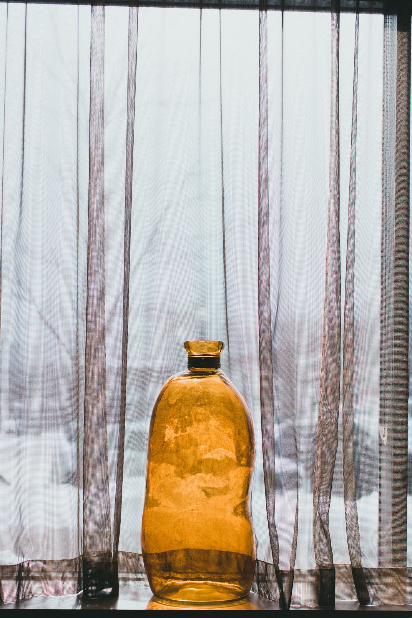 A skincare bottle on a table beside a bright window diffused by a sheer white curtain, lit by soft wrapping daylight