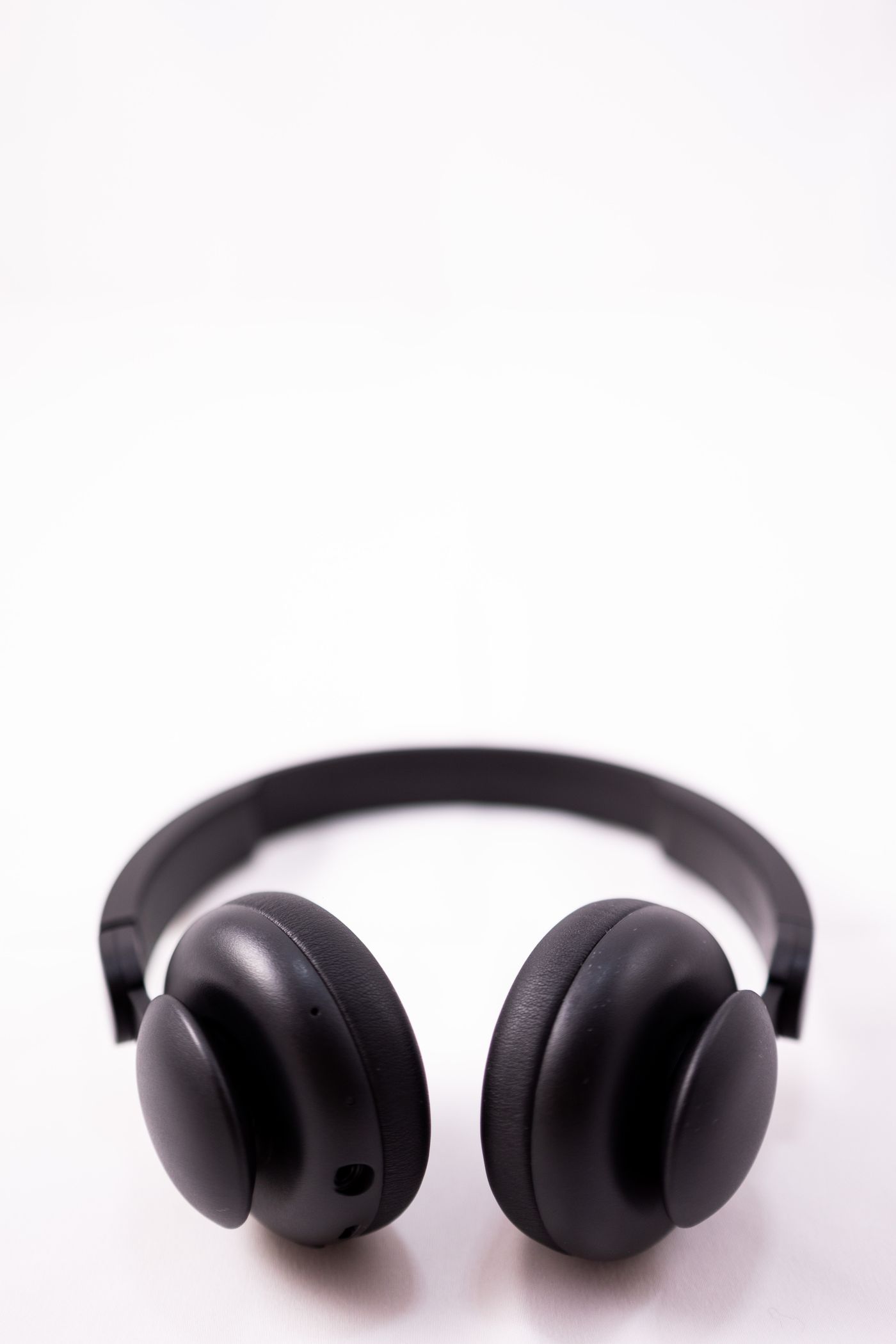 A pair of matte black over-ear headphones photographed alone on a plain white surface with a faint soft shadow and nothing else in the frame.