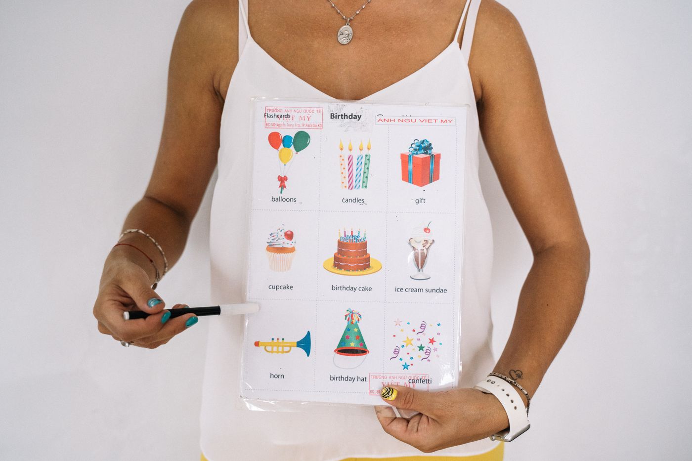 Hands holding up a colourful printed educational flashcard sheet covered in birthday-themed illustrations