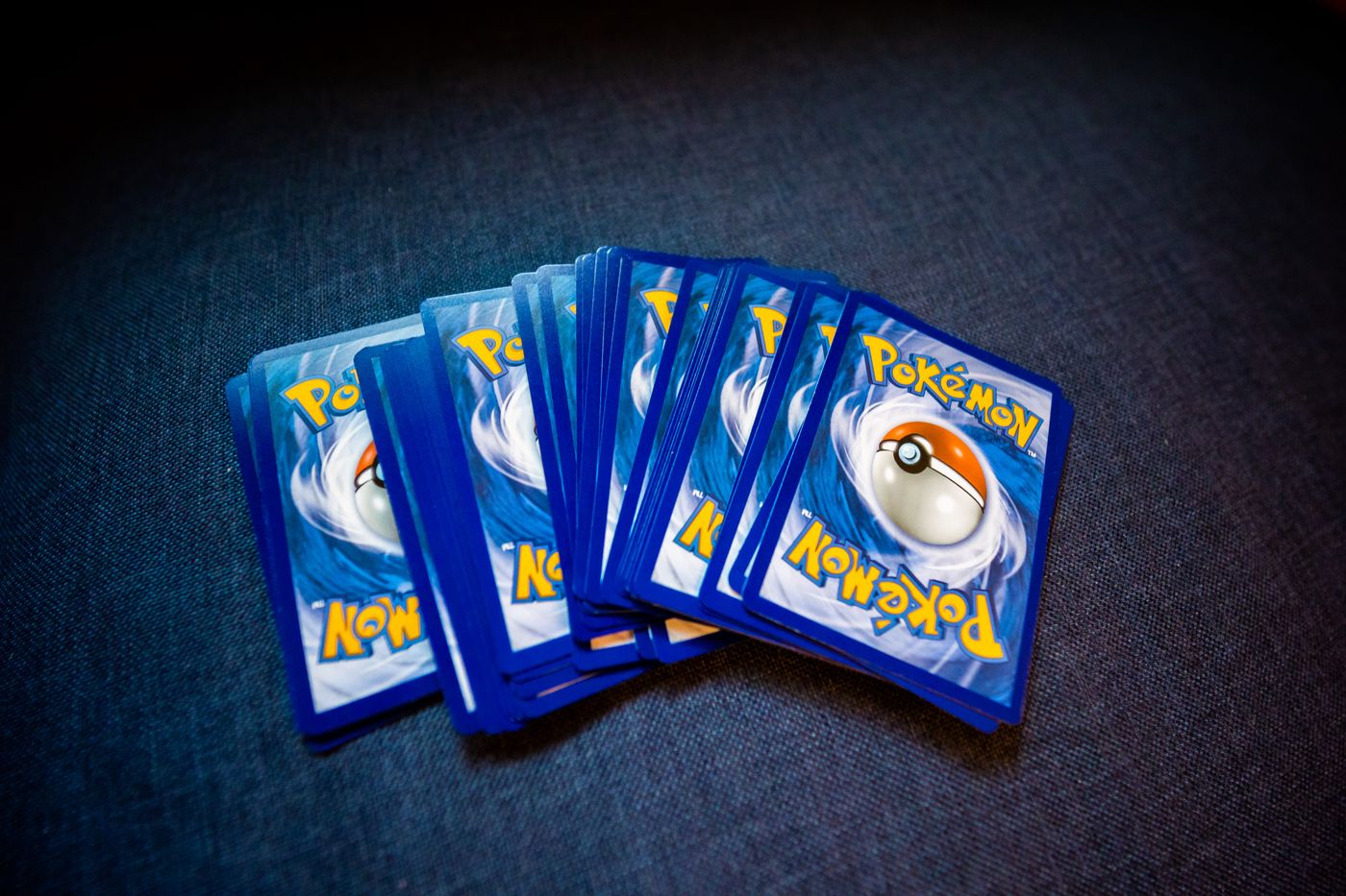Rozłożone wachlarzem karty Pokemon leżące rewersem do góry na ciemnej tkaninie, z niebieskim wzorem Poke Balla na każdej z nich