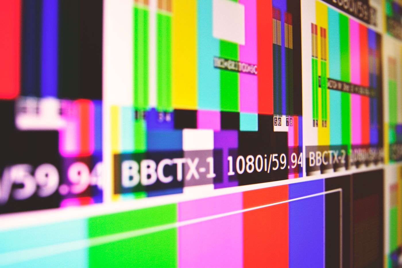 A wall of broadcast monitors displaying identical colour bar test patterns in saturated red, green, cyan and magenta stripes.