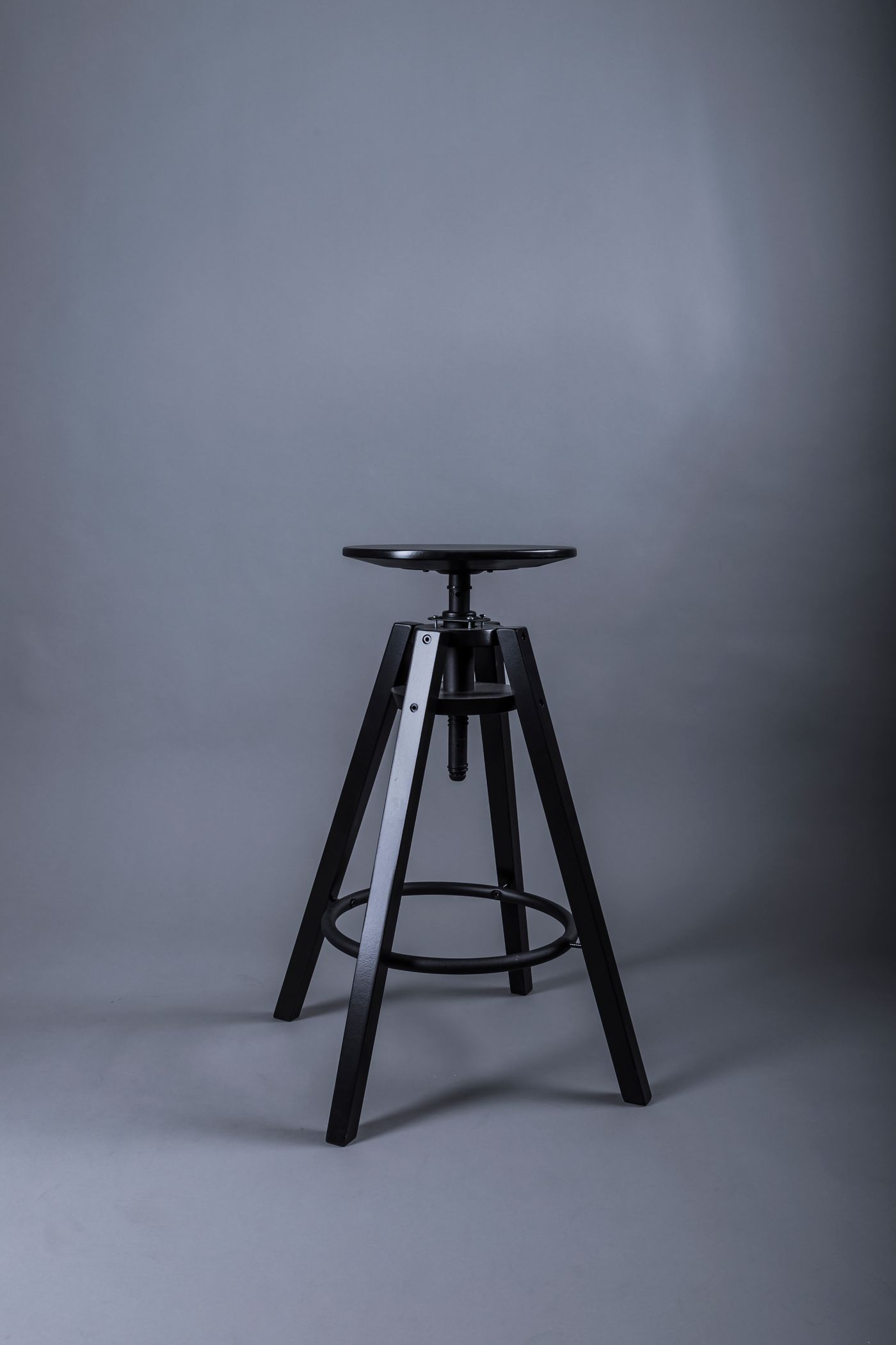Un semplice sgabello da bar nero con gambe di metallo, isolato su un fondale da studio neutro e uniforme, senza stanza né dintorni visibili.