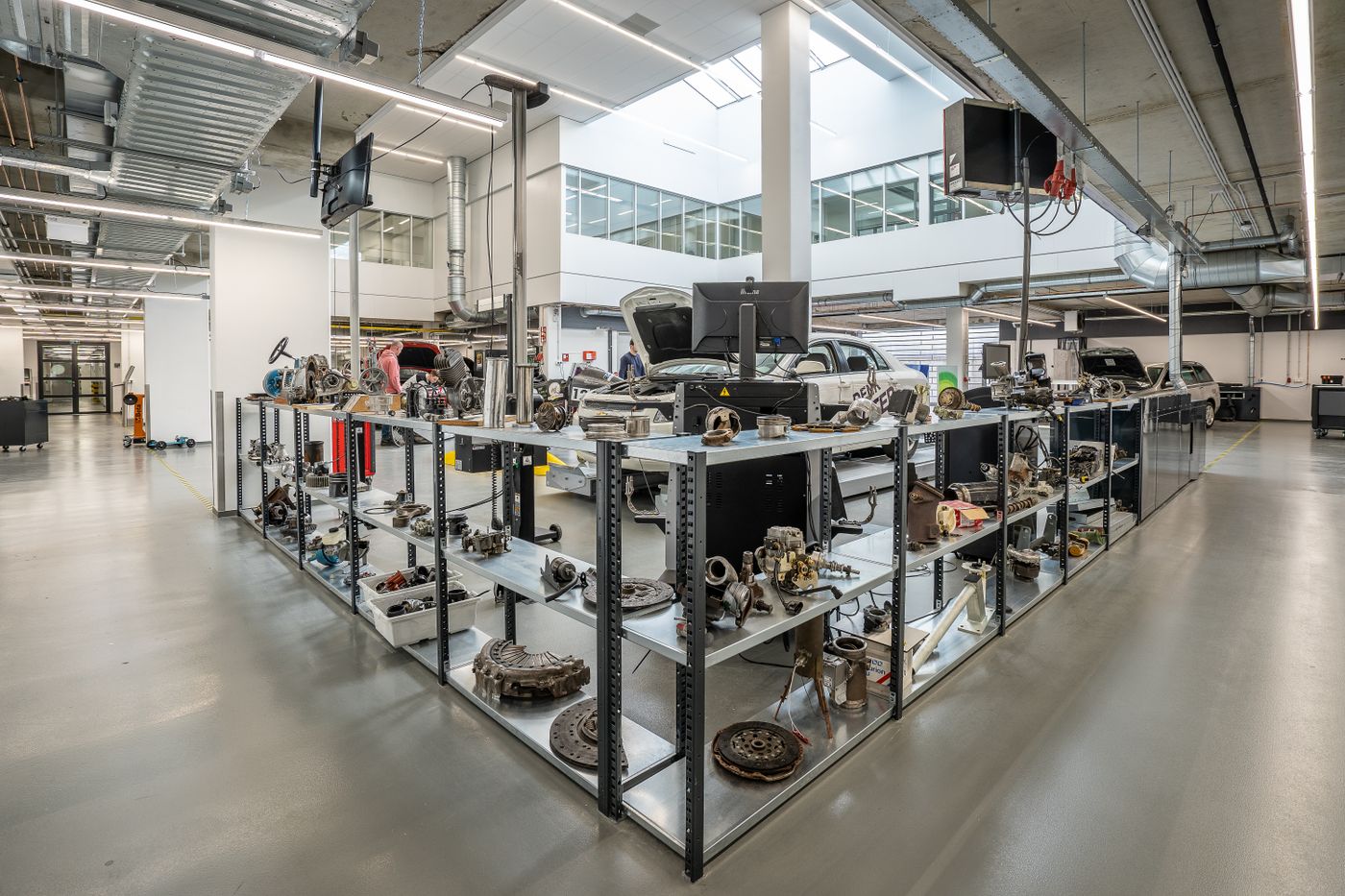 Rows of steel shelving in a bright workshop filled with dismantled engine and drivetrain parts arranged in neat, evenly spaced groups