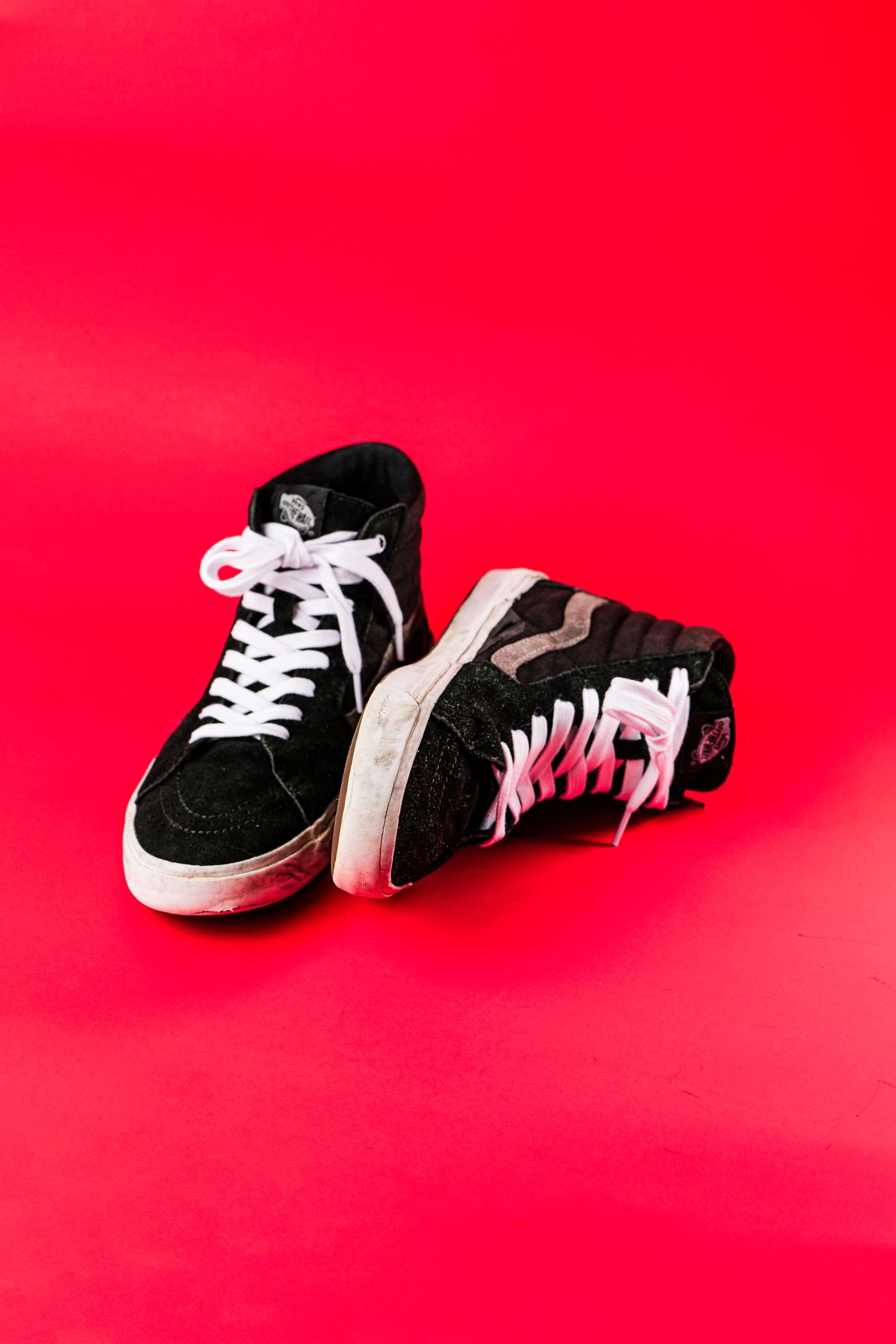 A pair of black high-top canvas sneakers standing on a flat, evenly lit red studio backdrop
