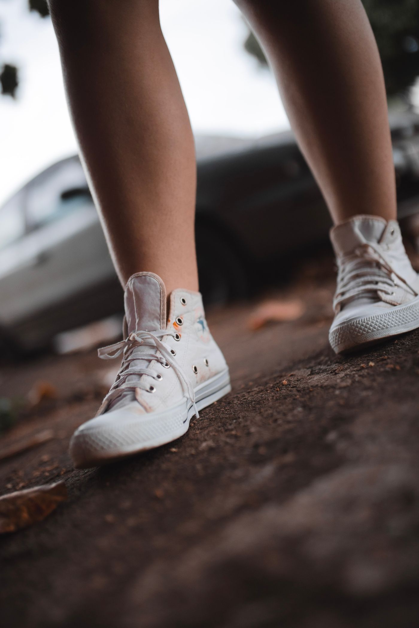 Close-up of white sneakers worn on a person's feet standing on a grey city pavement outdoors