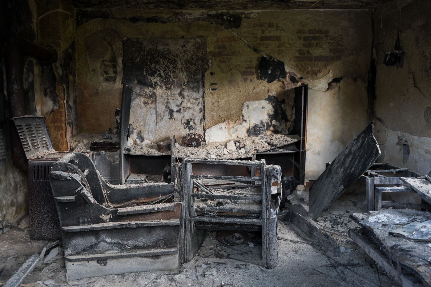 The burnt interior of a home, with charred chairs, soot-blackened walls and ash covering the floor in dim light