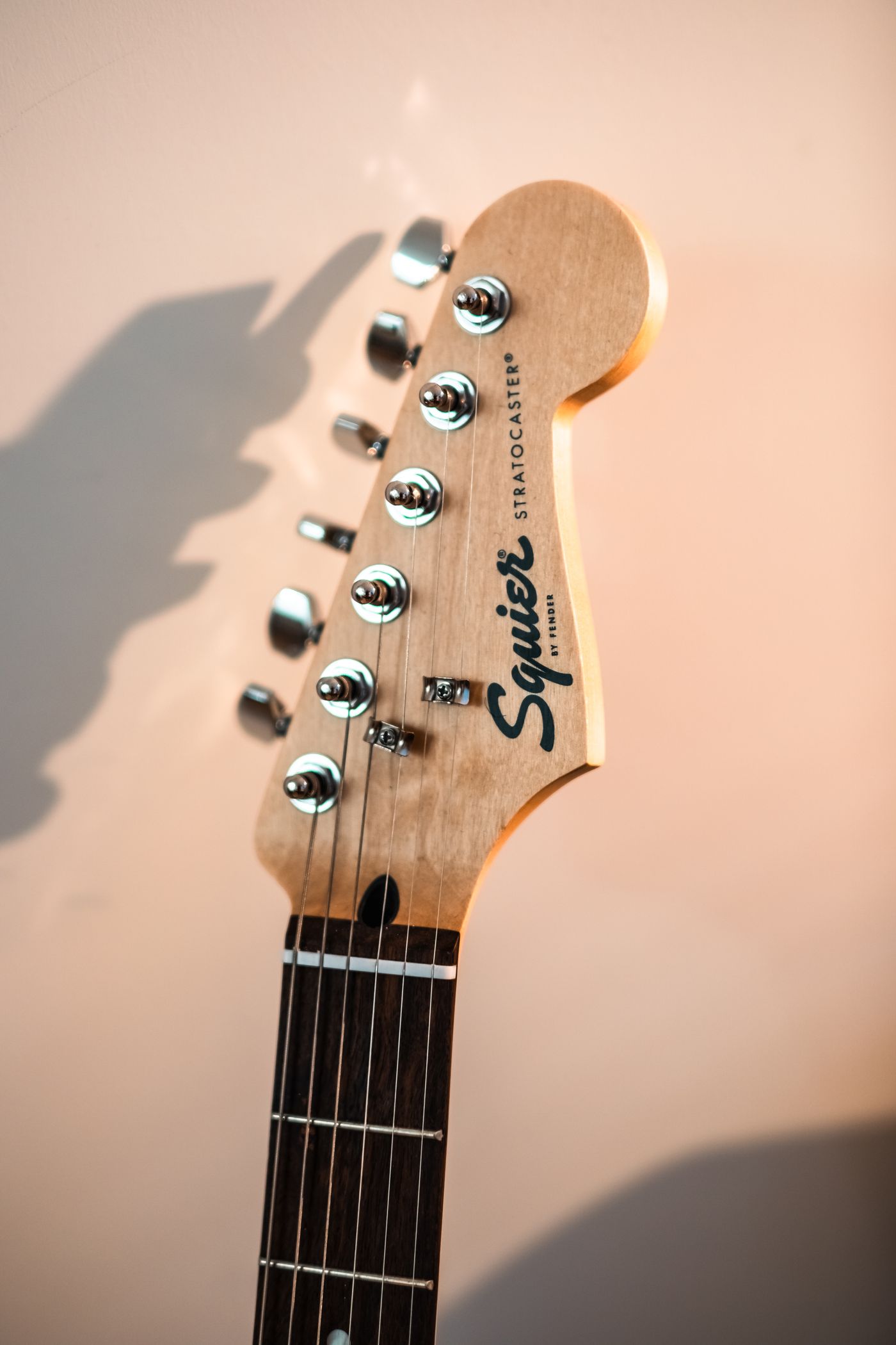 لقطة مقرّبة ماكرو لرأس جيتار Squier Stratocaster، يظهر فيها شعار العلامة التجارية ومفاتيح الضبط الستة بوضوح بينما تتلاشى الخلفية خارج نطاق التركيز.