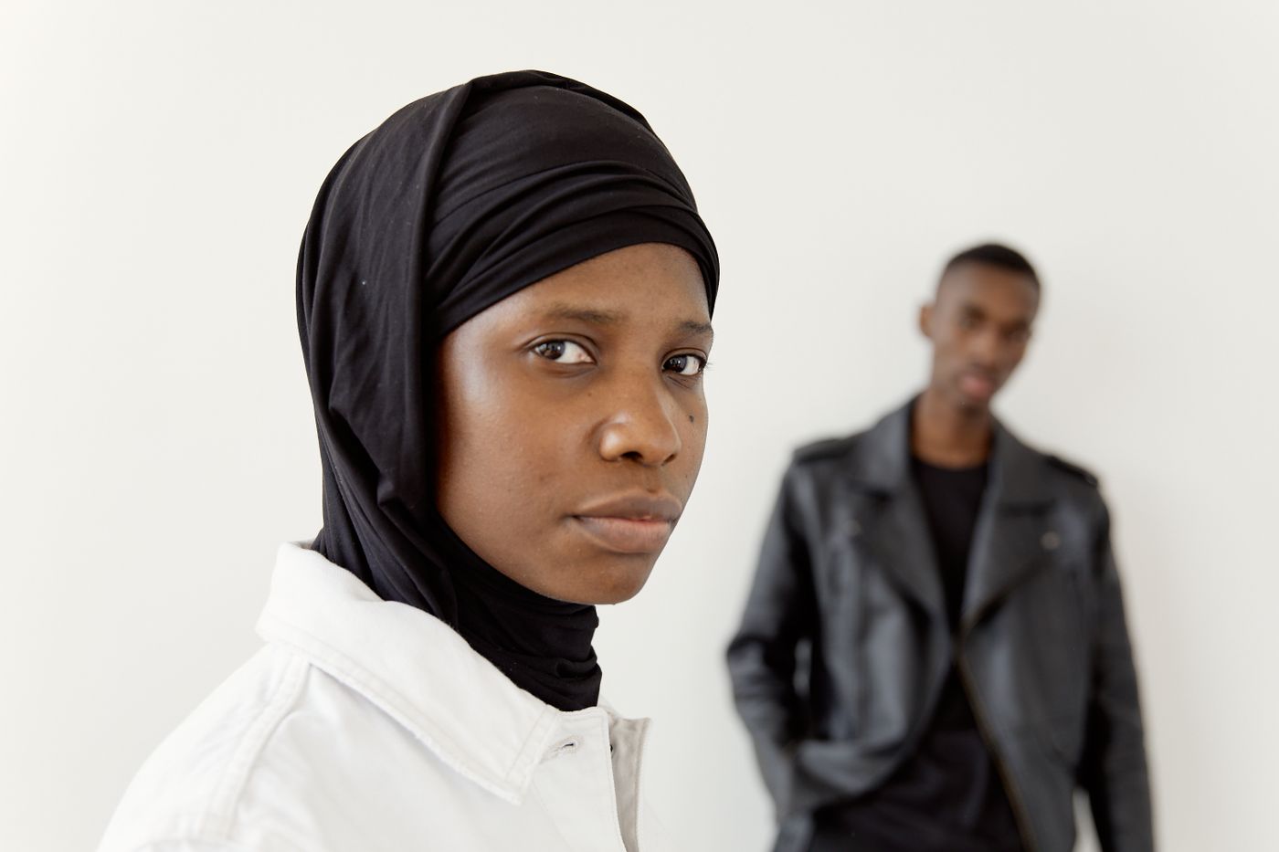 A woman in a black hijab in sharp focus in the foreground with a man out of focus behind her.